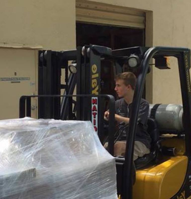 employee driving a forklift delivering clear-wrapped packages to a warehouse